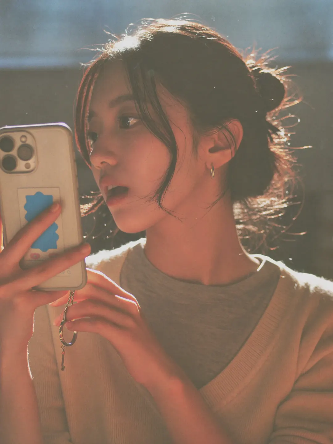 A woman in a cream sweater, her hair in a loose bun, talking into the phone she holds up with its back to the camera
