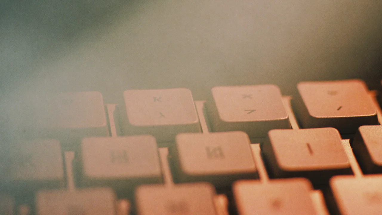 Close-up of rows of pale laptop keys in warm, hazy light, their faint markings soft and out of focus.