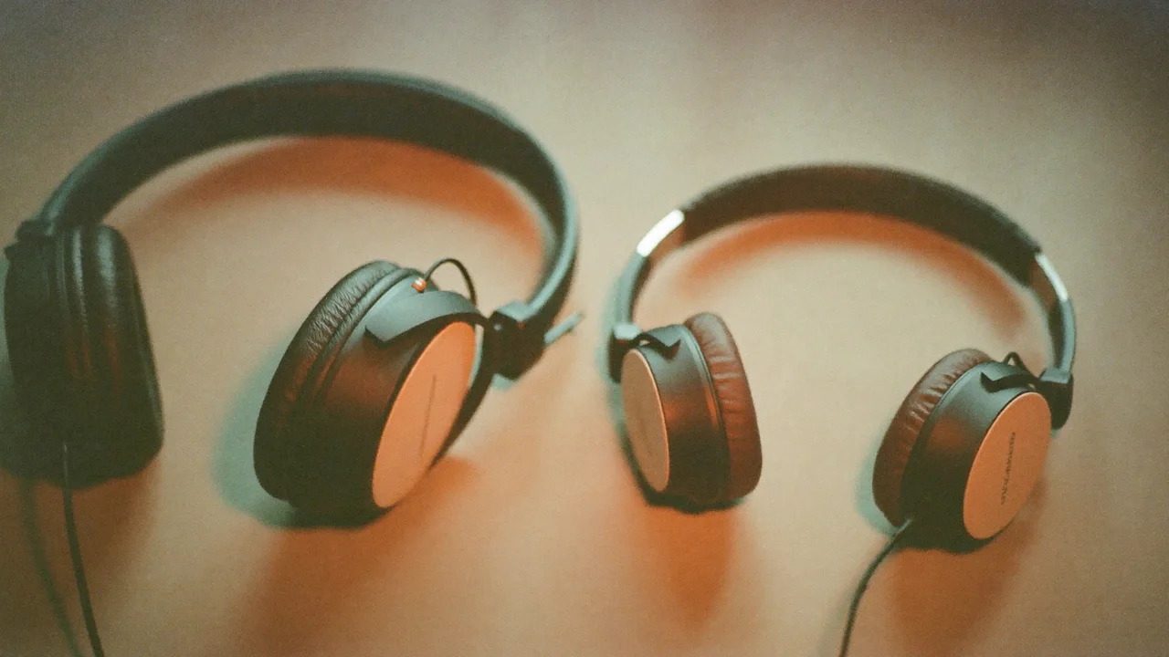 Two pairs of black on-ear headphones with copper-toned ear cups lie side by side on a warm-toned surface, their cables trailing out of frame.